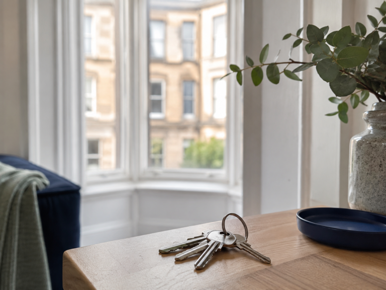 House keys on a wooden surface with an out-of-focus tenement bay window behind in morning light - Oracle Law Glasgow